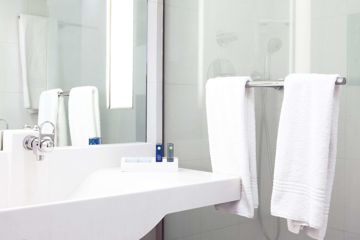 Une salle de bain moderne avec un lavabo blanc, un miroir et deux serviettes blanches suspendues à un porte-serviettes.