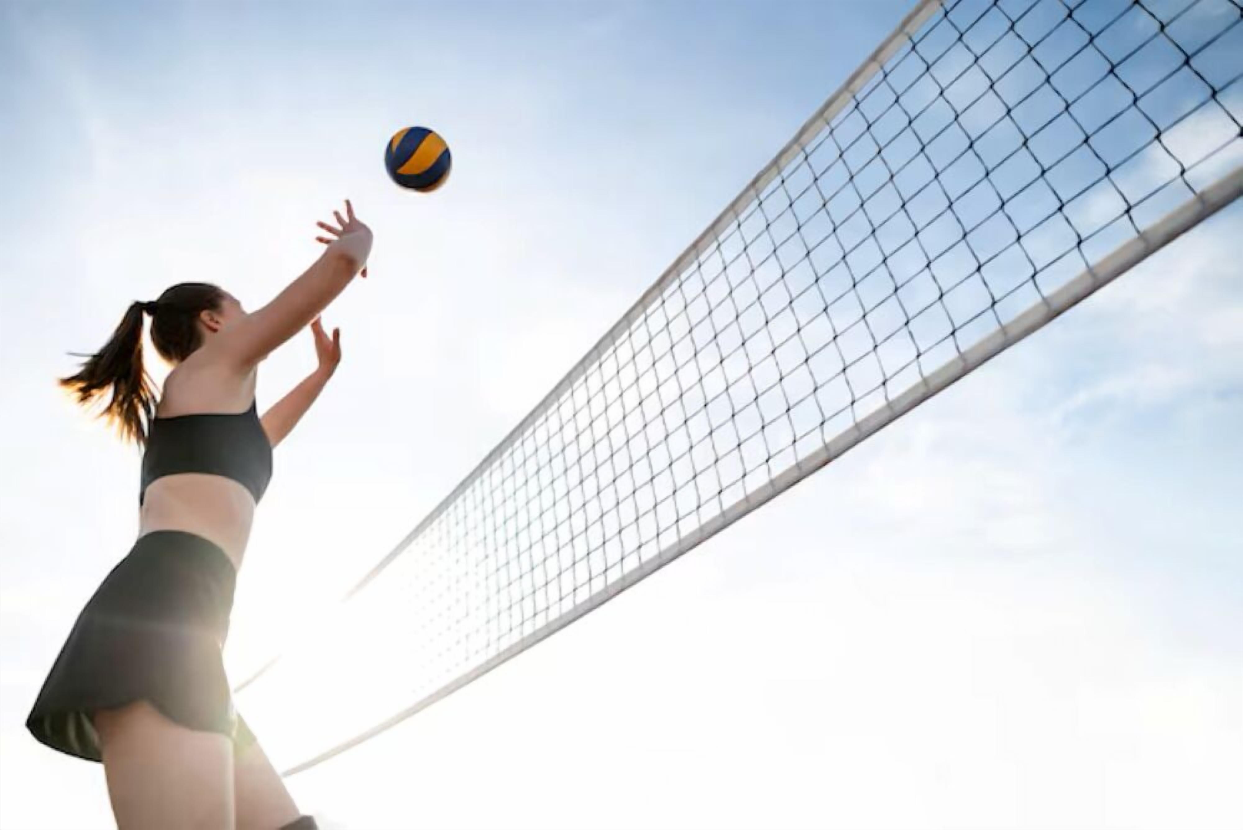 Un joueur de volleyball en plein mouvement, qui tend la main pour frapper le ballon au-dessus du filet.