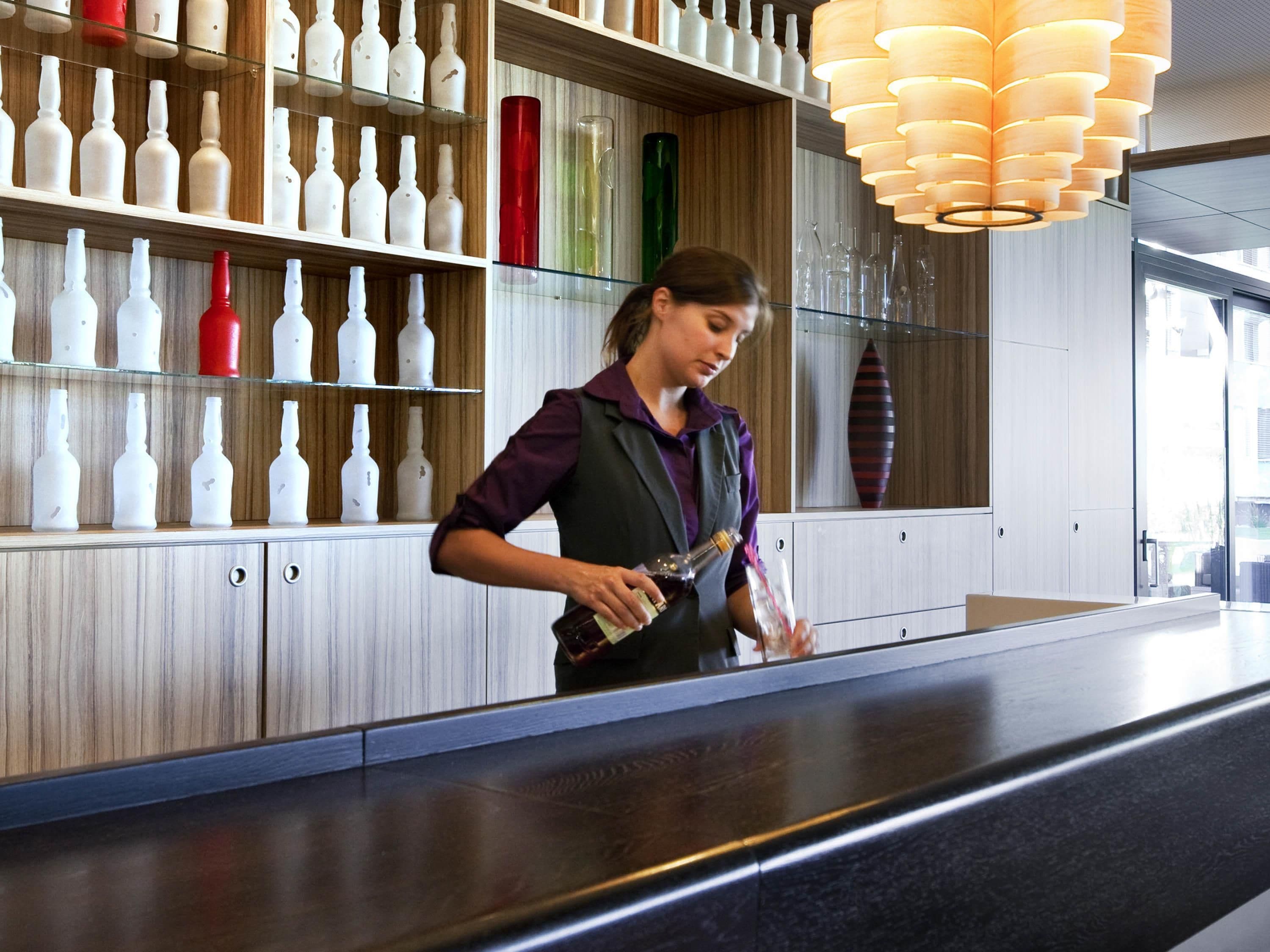 A bar area with a bartender, shelves with bottles, and a modern light fixture.