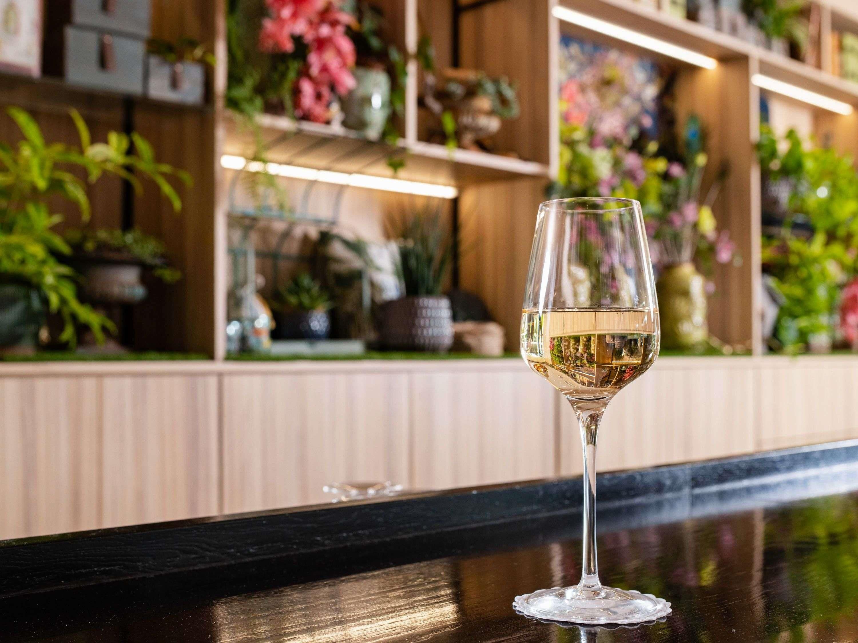 Een bar met een glas witte wijn, planten op planken en houten lambrisering.