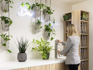 A modern interior with hanging planters, a neon sign, a water dispenser, and a wooden shelf with glass bottles.
