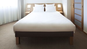 A neatly made bed with white linens and a wooden headboard, flanked by bedside tables with lamps.