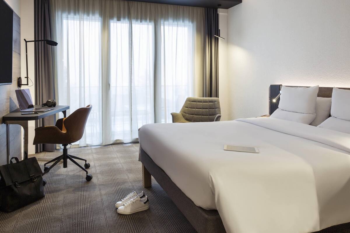 A hotel room with a bed, a desk with a laptop, a chair, and a suitcase on the floor.
