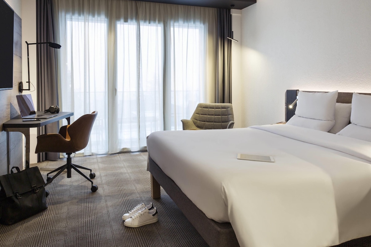 A hotel room with a bed, a desk, a chair, and a suitcase on the floor.
