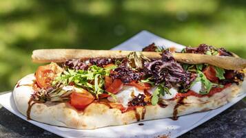 Een platbrood met toppings, een houten stokje en een wit bord op een tafel.