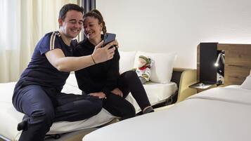 Une chambre d’hôtel avec un lit, un canapé, une table de chevet avec une lampe et un jouet en peluche posé sur le canapé.
