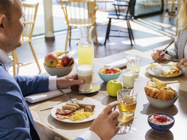 A breakfast setting with a variety of food items, including eggs, sausages, and pastries, on a table with a glass of juice and a bowl of fruit.