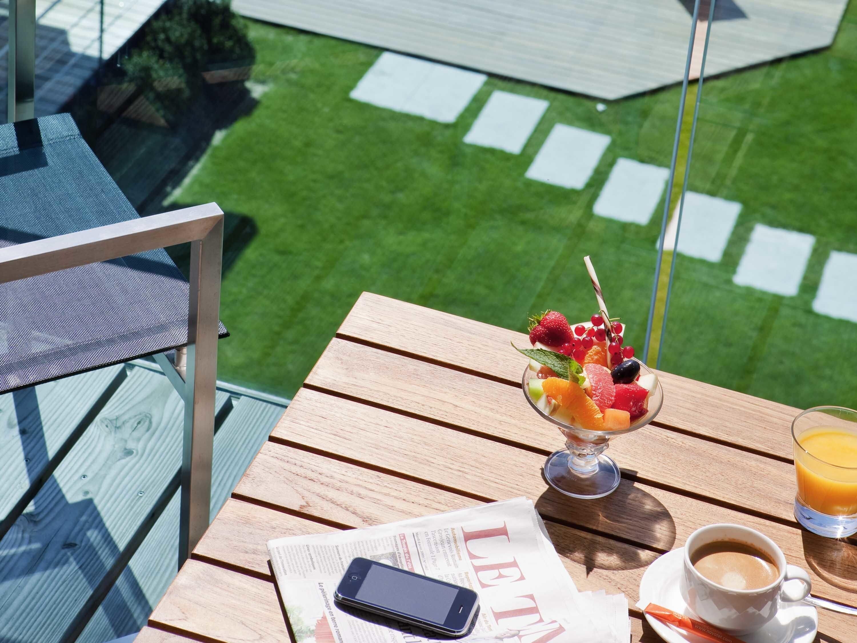 Une table en bois avec un dessert aux fruits, un verre de jus d’orange, une tasse de café et un journal.