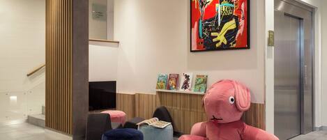 A modern lobby with a large abstract painting, a plush pink elephant, and a staircase.