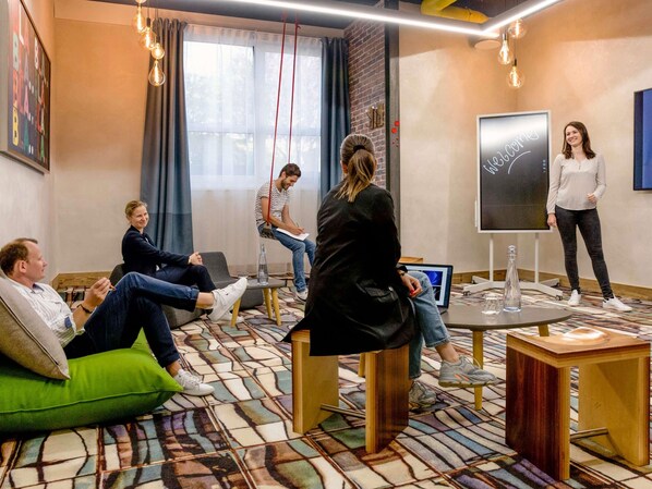 Uma sala de reuniões moderna com um ecrã grande, assentos confortáveis e um chão estampado.