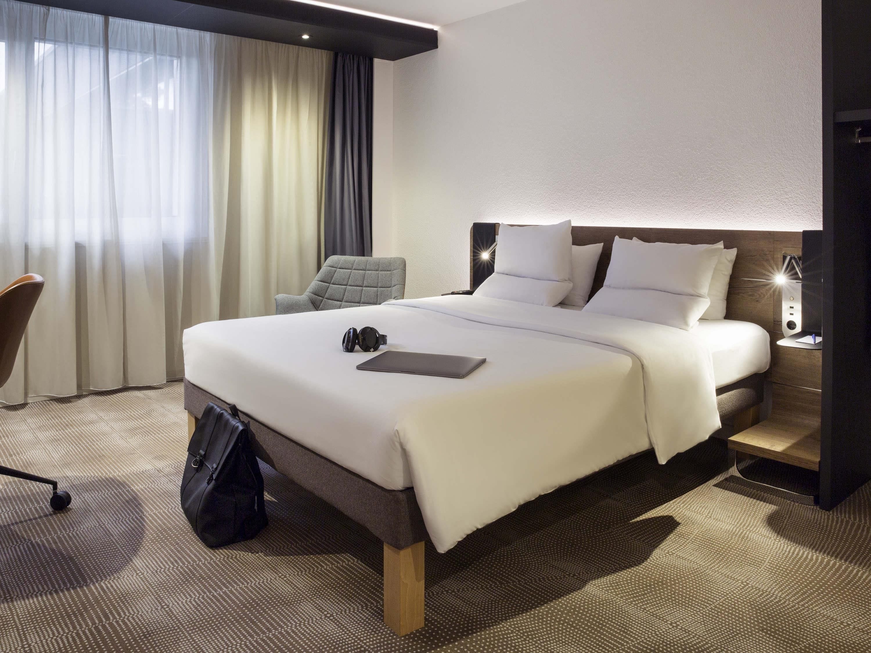 Habitación de hotel con una cama grande, una silla, un escritorio con lámpara y una ventana con cortinas.