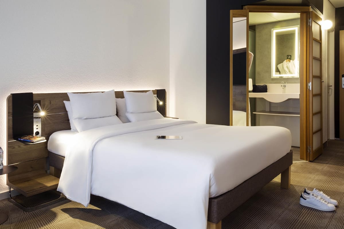 A hotel room with a bed, bedside table, lamp, and a mirror.