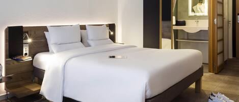 Habitación de hotel con cama, mesita de noche, lámpara y espejo.