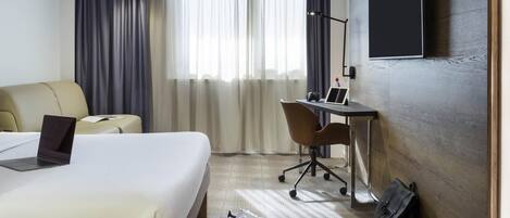 A hotel room with a bed, a desk, a chair, a laptop, a TV, and a bag.