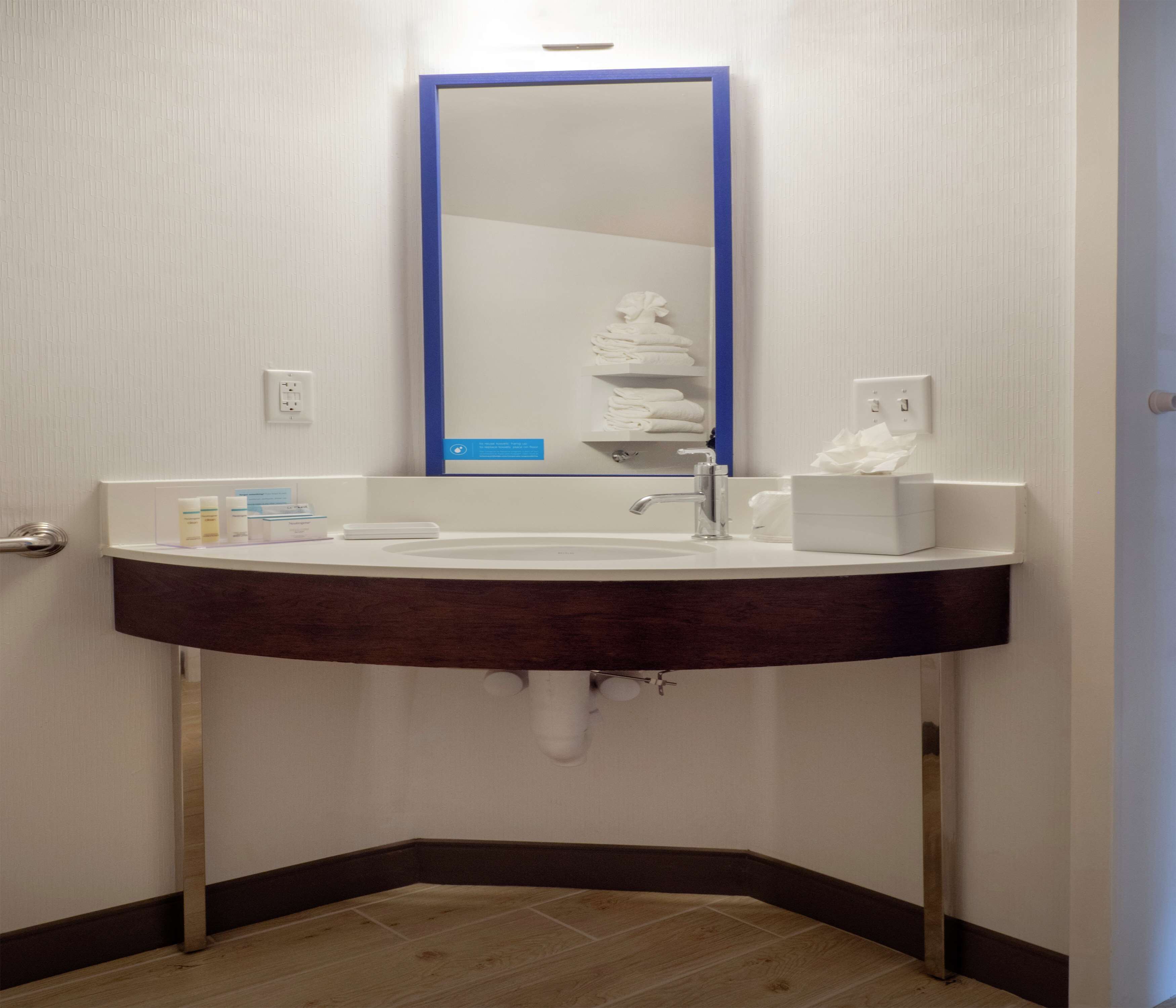 Une salle de bain avec un lavabo blanc, un miroir à cadre bleu et un porte-serviettes avec des serviettes pliées.