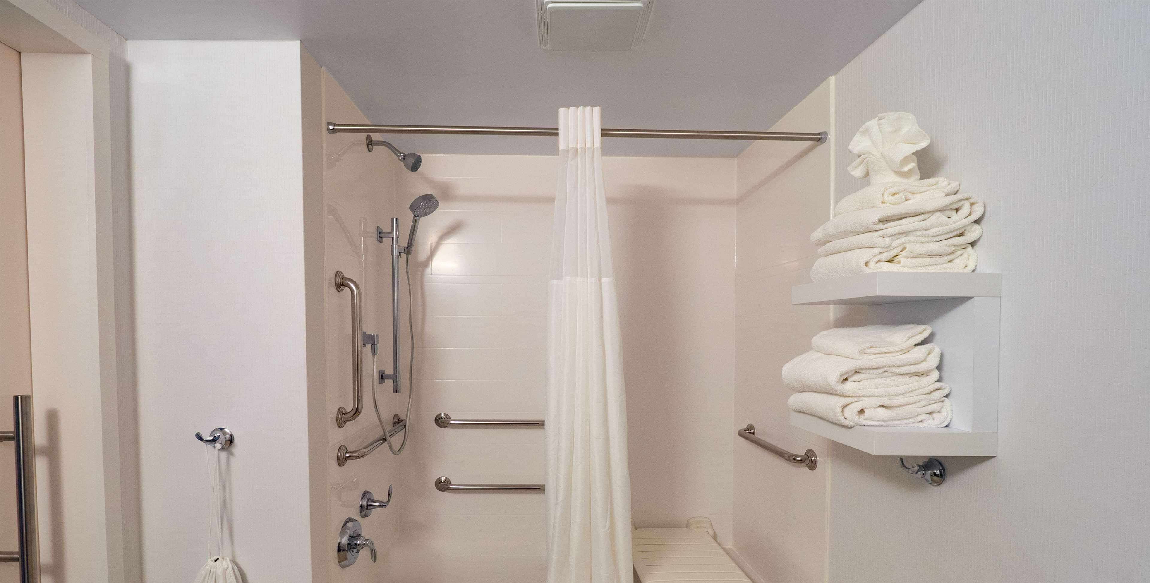 A modern bathroom with a shower, grab bars, and a towel rack.