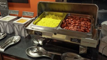 Un buffet proposant des œufs brouillés, des saucisses et du riz.