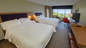 A hotel room with two beds, a desk, a chair, a TV, and a window with a mountain view.