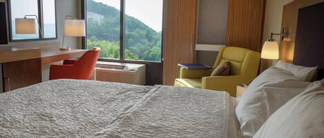 A hotel room with a large bed, a desk with a chair, a sofa, and a view of a mountain.