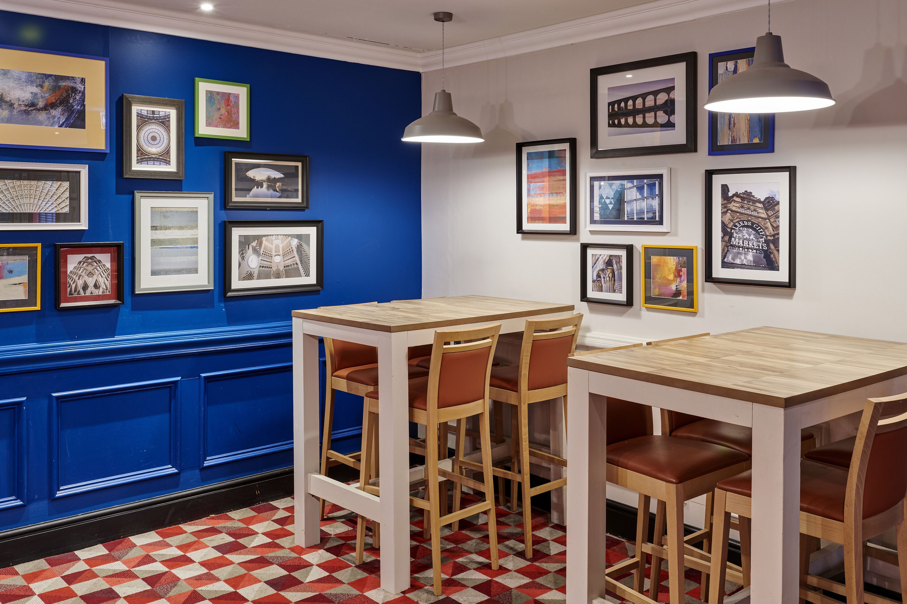 A restaurant interior with a blue accent wall, framed artwork, wooden tables and chairs, and a checkered floor pattern.
