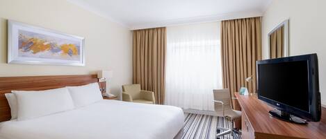 Une chambre d’hôtel avec un grand lit, un bureau avec une télévision, une chaise et un tableau au mur.
