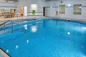 A large indoor swimming pool with a tiled floor and a metal ladder.