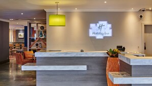 A modern hotel reception area with a wooden reception desk, a green pendant light, and a 'Holiday Inn' sign. - Holiday Inn Leeds Garforth by IHG (Leeds)
