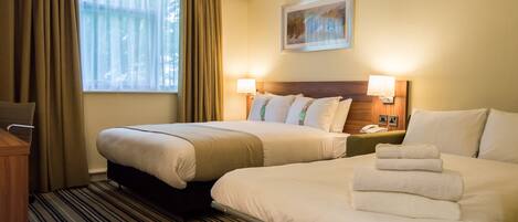 A hotel room with two beds, a window with curtains, a painting on the wall, and a bedside table with a lamp.