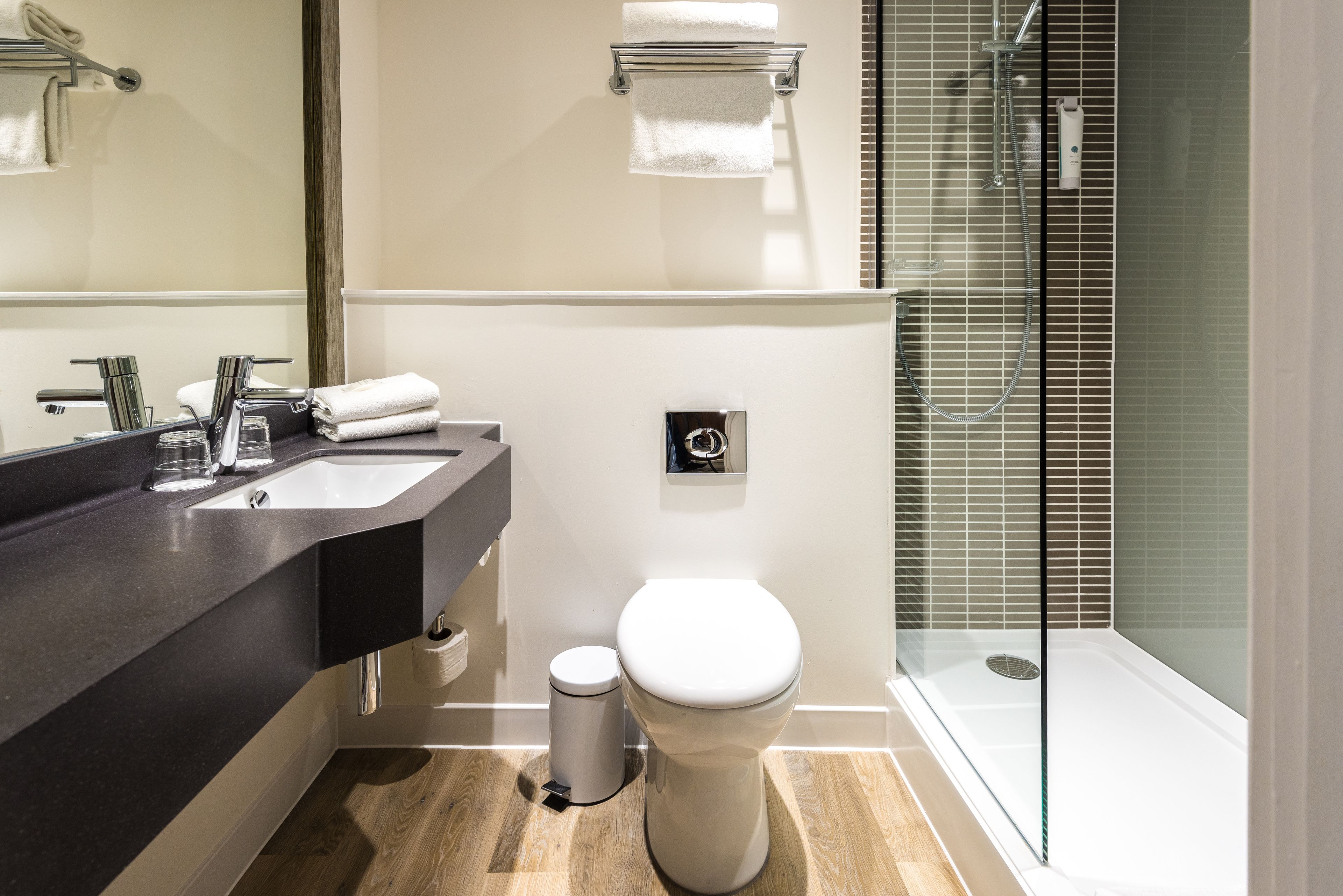 A modern bathroom with a dark countertop, a white toilet, and a glass shower enclosure.