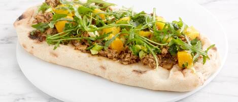 A flatbread with meat and vegetables on a white plate.