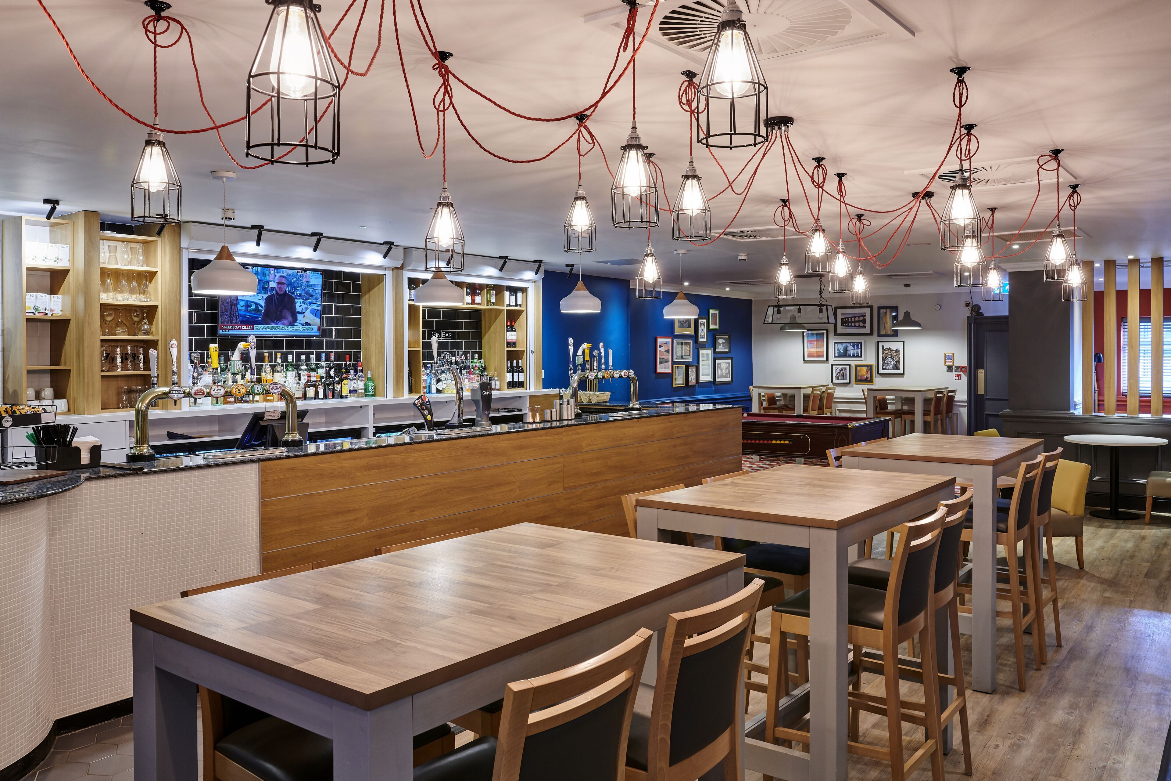 A restaurant with wooden tables and chairs, a bar area, and hanging pendant lights.
