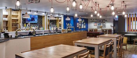 A restaurant with wooden tables and chairs, a bar area, and hanging pendant lights.