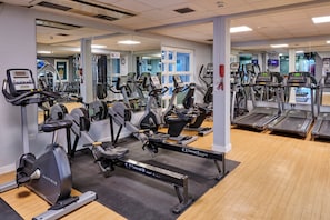 Une salle de sport équipée de plusieurs appareils de cardio, de miroirs et d’un plancher en bois.