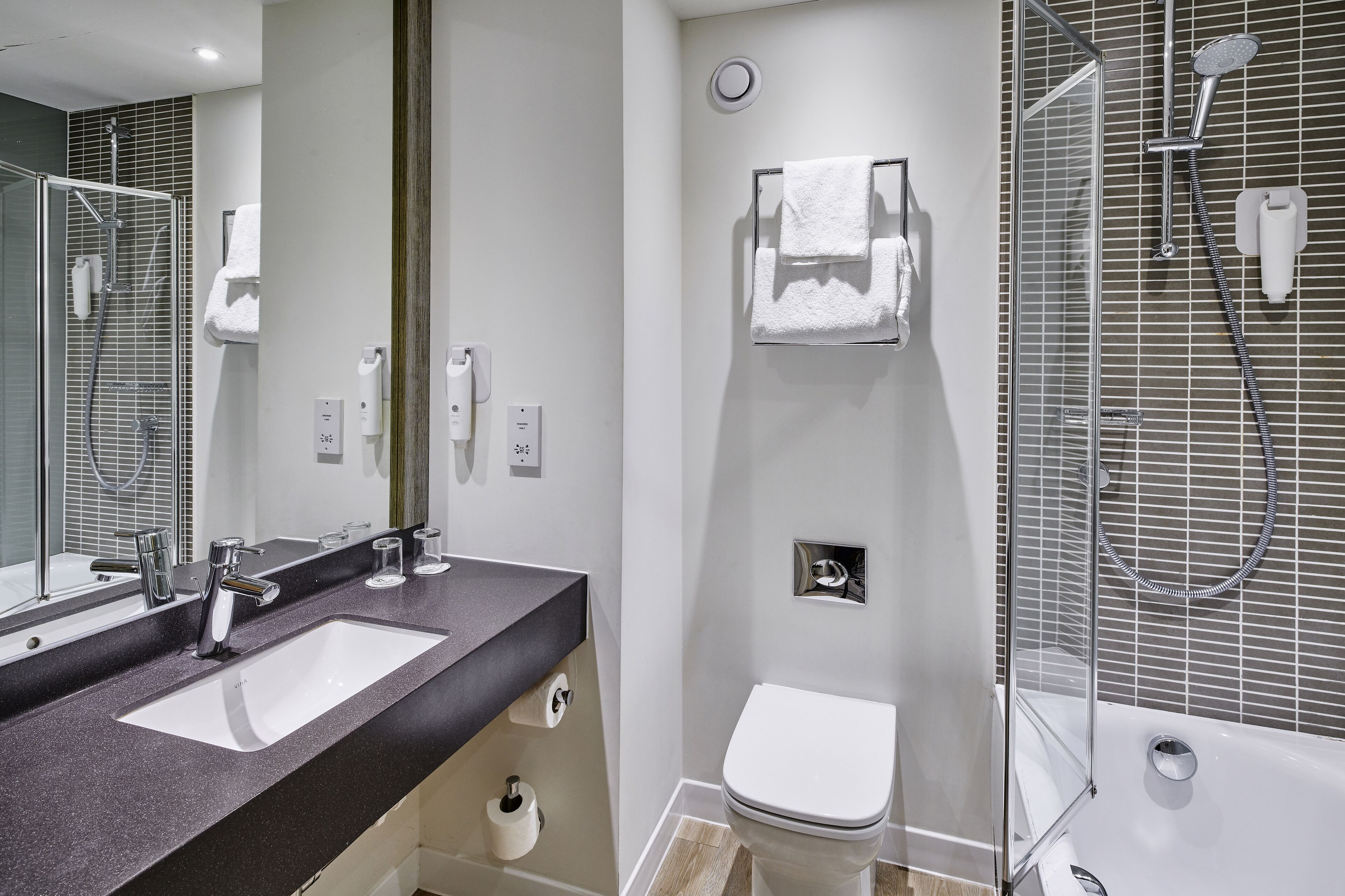 Une salle de bain moderne avec deux lavabos, des toilettes et une douche, le tout dans un espace de douche délimité par des parois en verre.