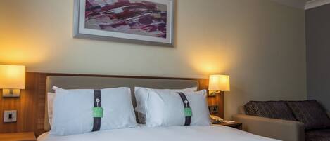 A hotel room with a large bed, two bedside lamps, a framed abstract painting, and a patterned throw on the bed.