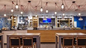 A modern bar area with wooden tables and chairs, a bar counter with a variety of bottles, and hanging light fixtures. - Holiday Inn Leeds Garforth by IHG (Leeds)