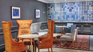 A modern lounge area with tufted chairs, a round table, and a patterned wall. - Holiday Inn Leeds Garforth by IHG (Leeds)