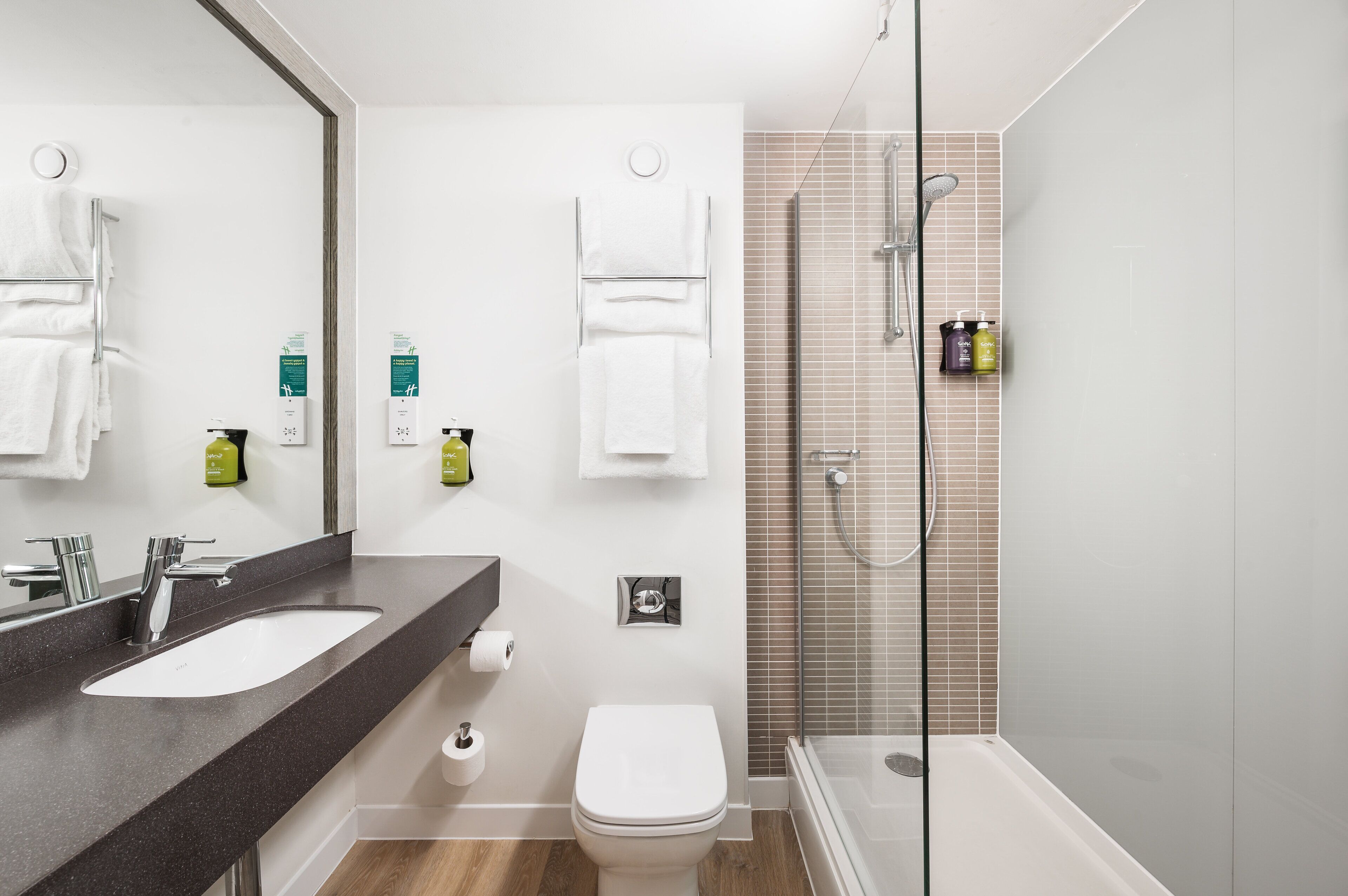 Un baño moderno con un espejo grande, un lavabo, un inodoro y una zona de ducha con mampara de vidrio.
