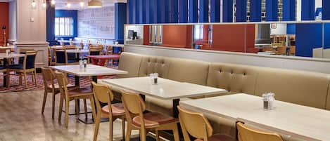 Un restaurante con mesas y sillas de madera, una zona central de estar con un banco acolchado, y una decoración con motivos azules y rojos.