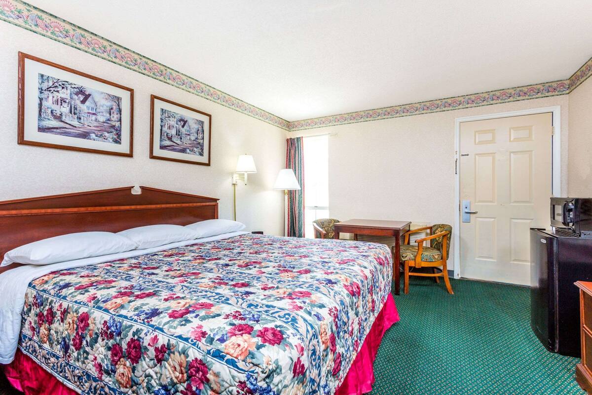 A hotel room with a bed, a desk, a chair, a television, and two framed pictures on the wall.