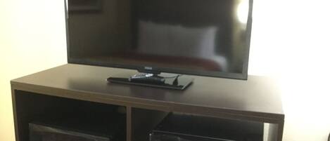 Un televisor de pantalla plana sobre un mueble de madera con un microondas y un refrigerador pequeño debajo.