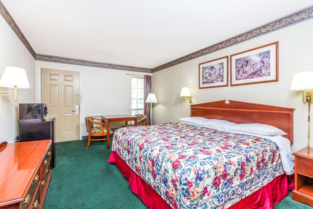 A hotel room with a large bed, a desk, a chair, and two framed pictures on the wall.