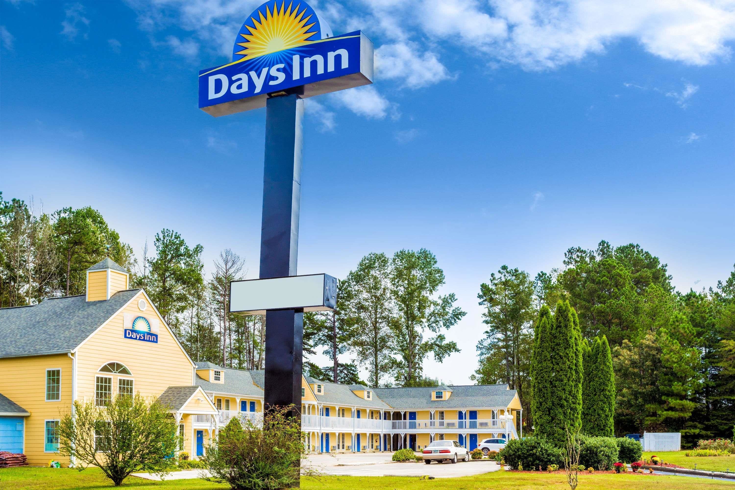 Un hotel Days Inn amb un cartell ben visible, edifici de color groc amb accents blaus i un jardí ben cuidat.