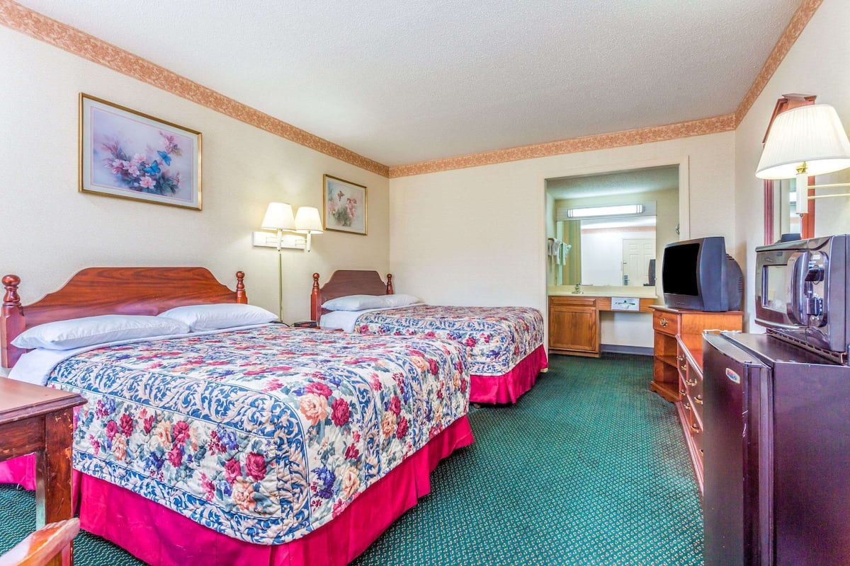 A hotel room with two beds, a desk with a television, a dresser, and a mirror.