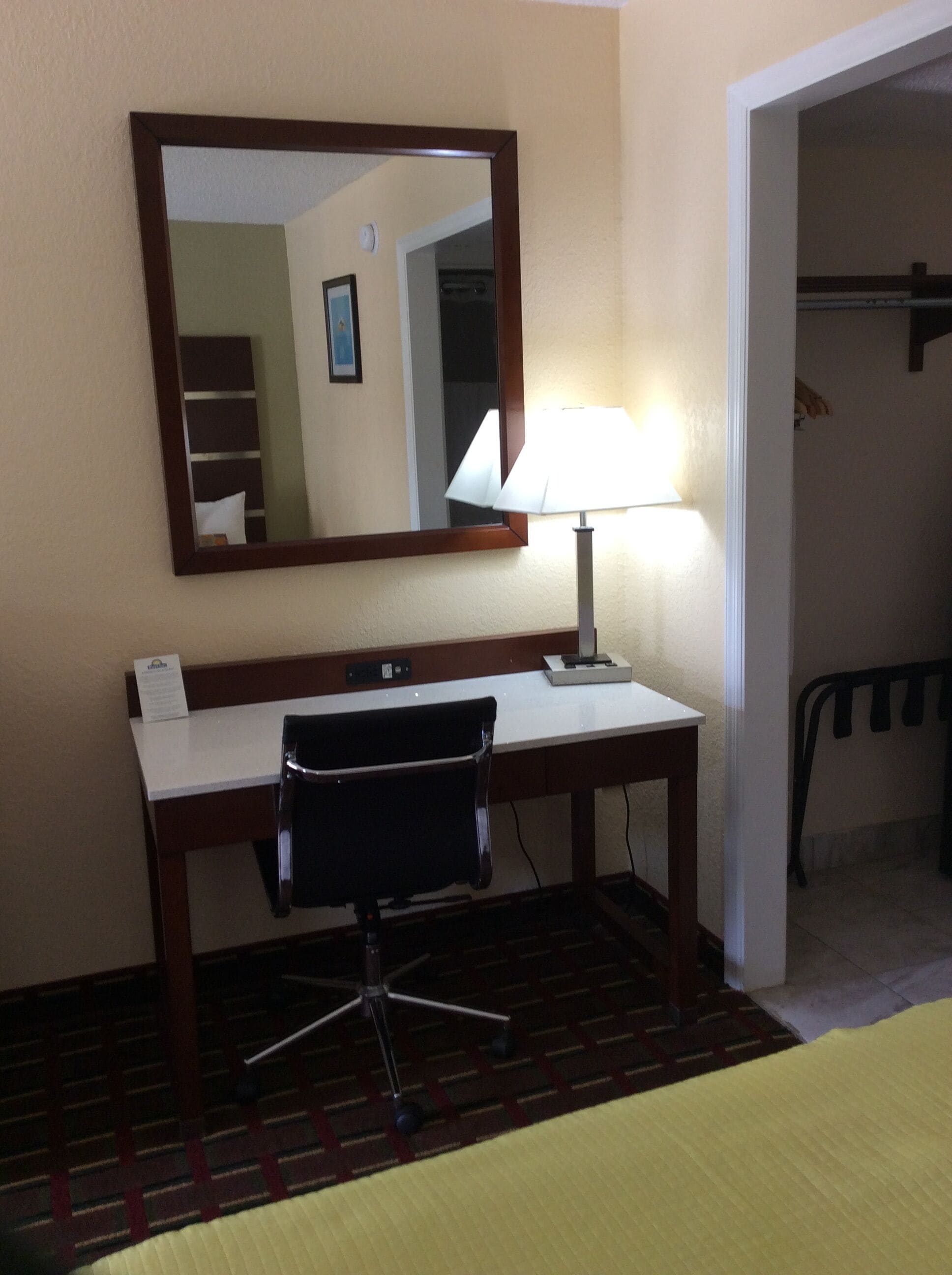 Una habitación de hotel con escritorio, silla, lámpara y espejo.