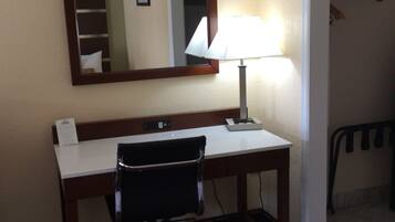 A hotel room with a desk, chair, lamp, and a mirror.