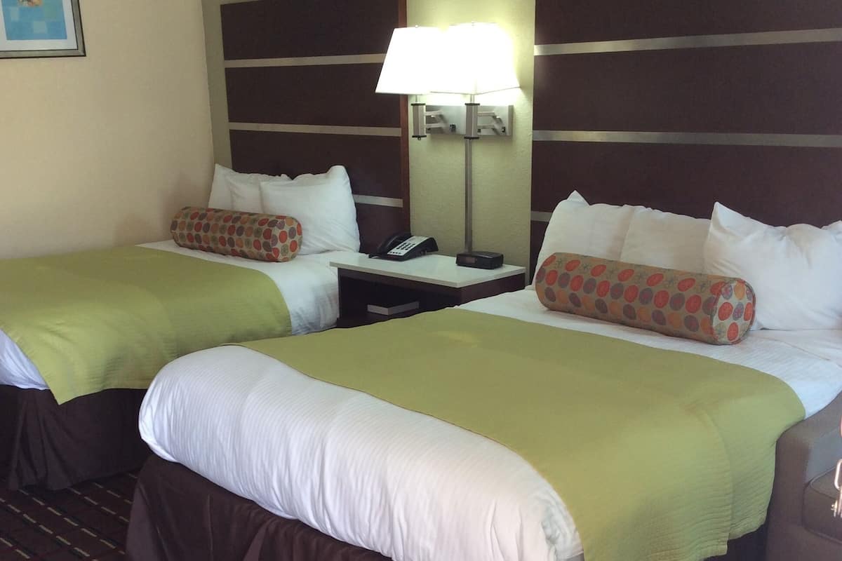 A hotel room with two beds, a nightstand, a lamp, and a telephone.