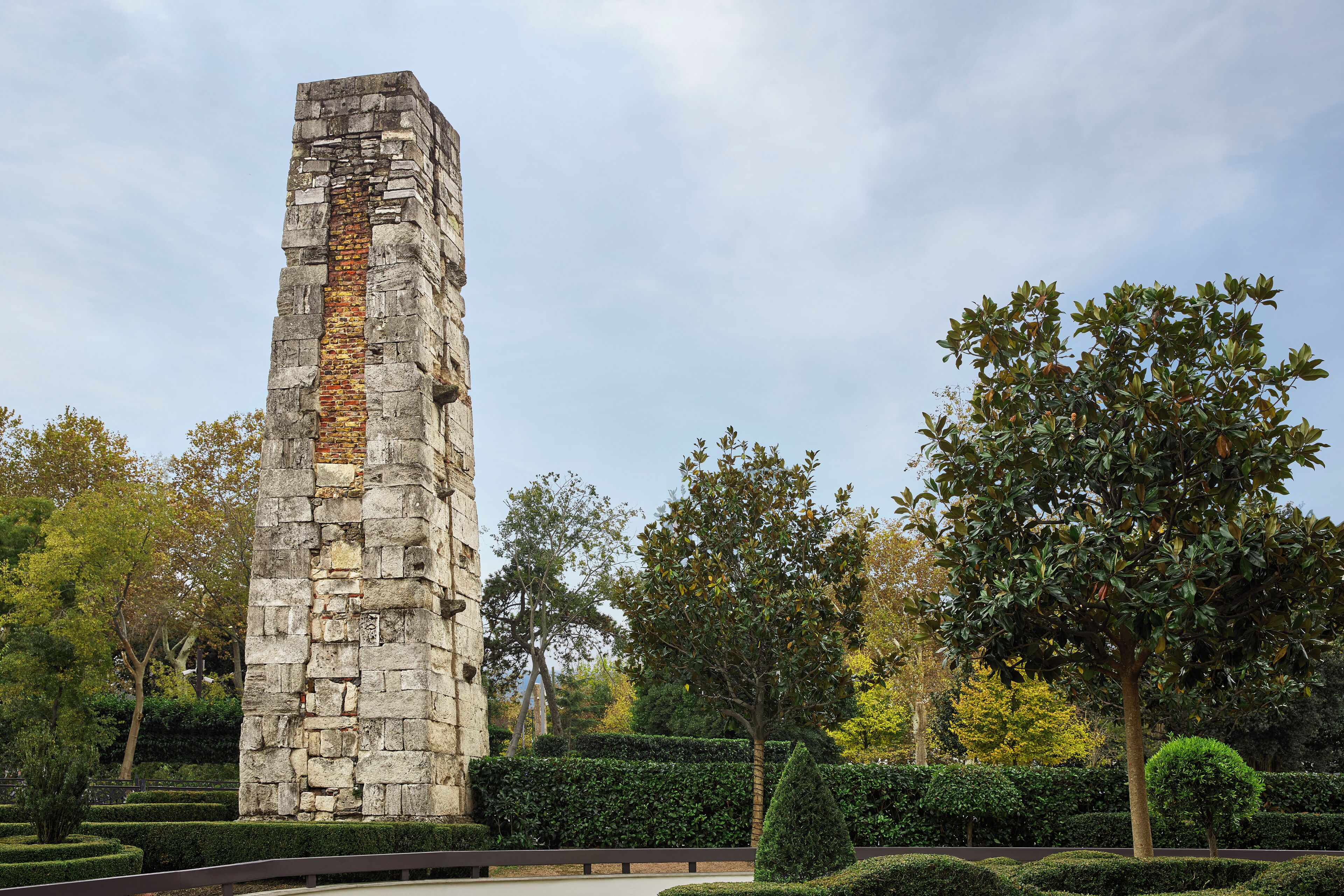 A tall stone monument surrounded by well-manicured hedges and trees.