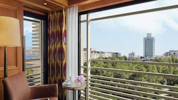 A hotel room with a large window, a chair, a small table with a vase, and a view of a cityscape.