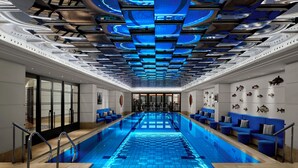 A modern indoor swimming pool with a blue-lit ceiling, seating areas, and fish wall decorations. - Divan Istanbul (Istanbul)